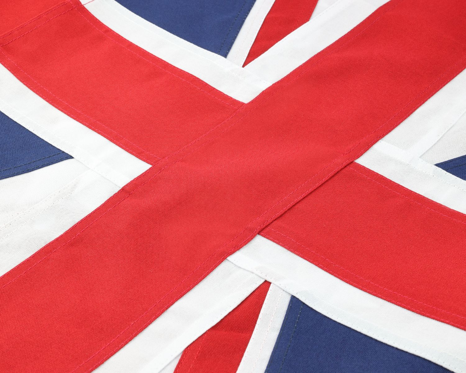 Close-up of a Union Jack flag fabric showing the red, white, and blue pattern with visible stitched seams and textile texture.